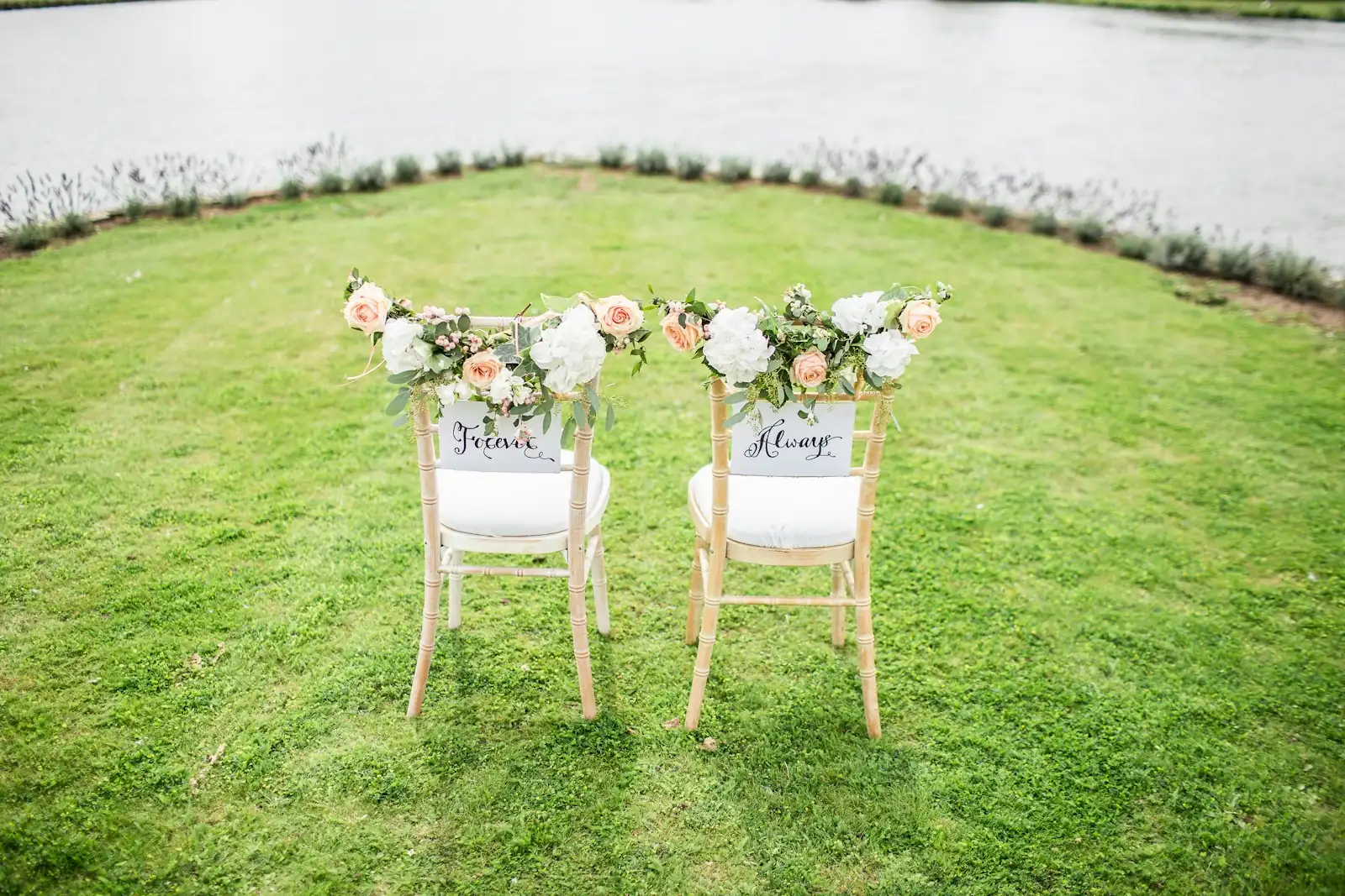 Two decorated chairs set for a wedding ceremony by the water